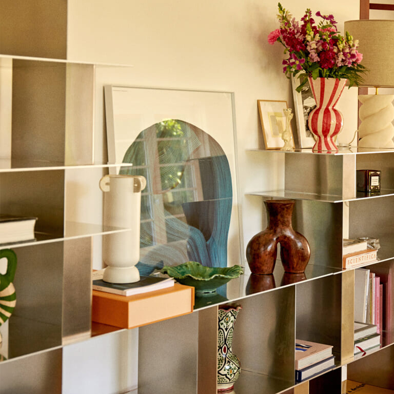 A modern modular shelf filled with decorative objects, vases, framed art, and a bouquet of pink flowers.