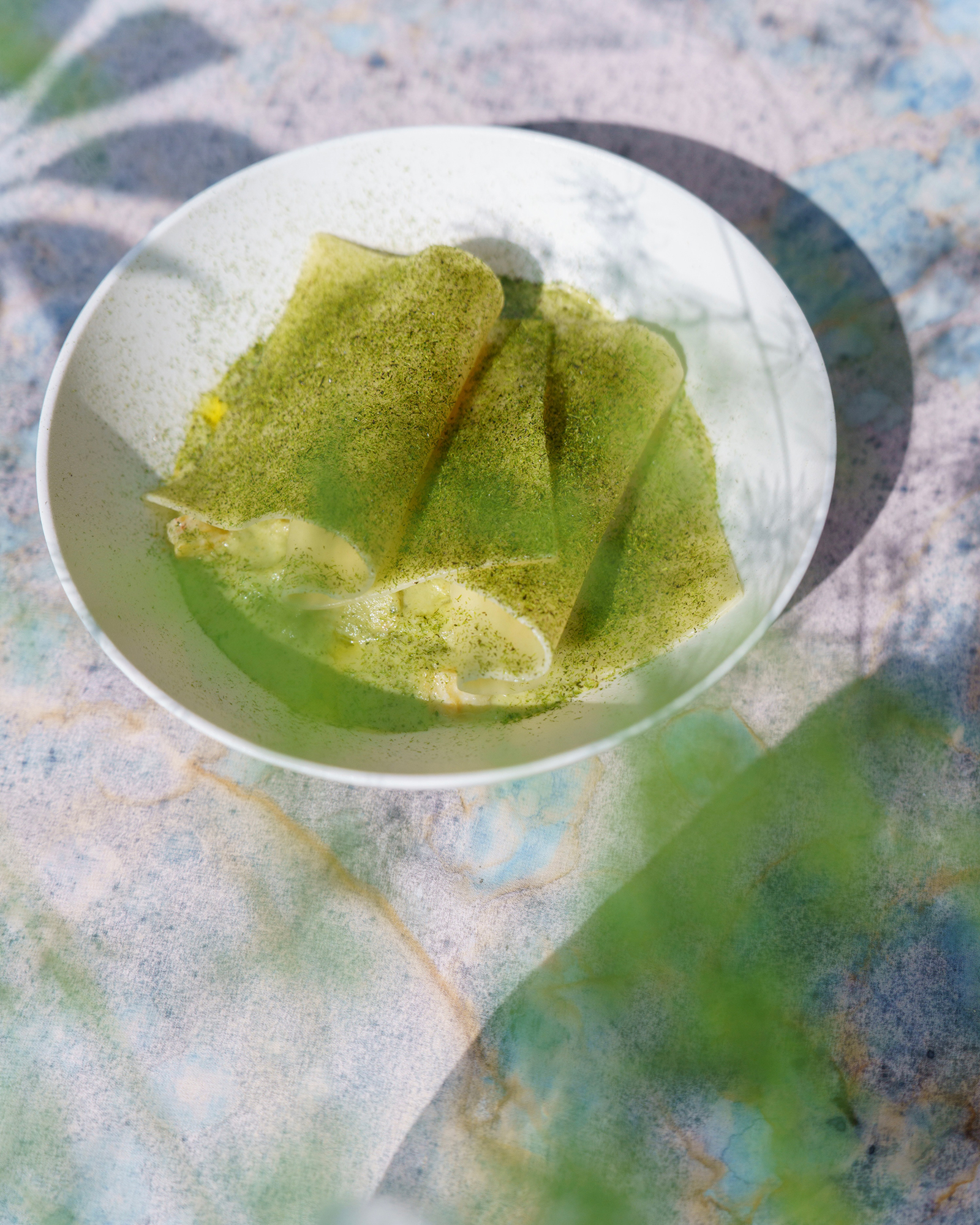 White bowl holding folded green tea crepes dusted with matcha on a colorful tablecloth
