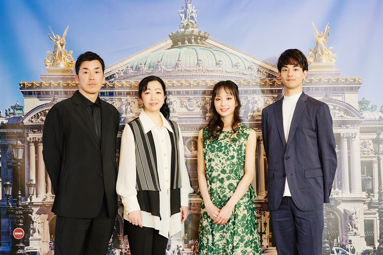 Four adults in formal clothing posing together in front of a grand building backdrop resembling an opera house.