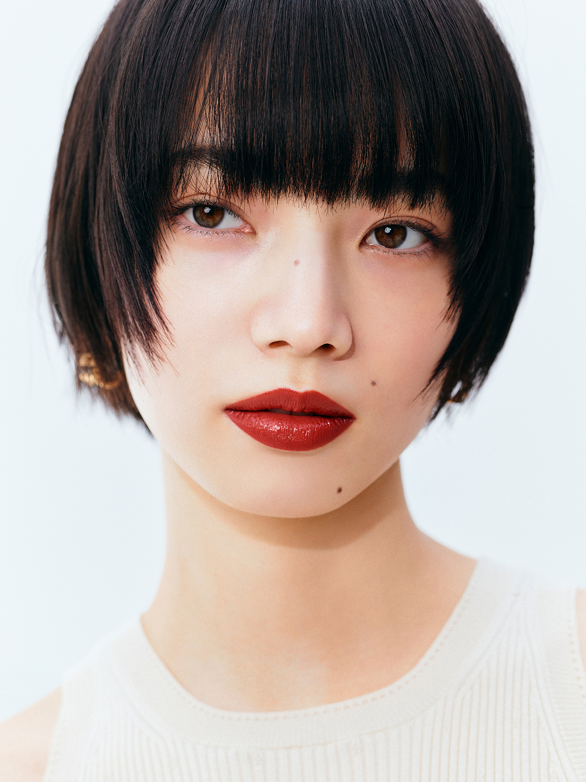 Close-up portrait of a woman with a short black bob and bold red lipstick against a pale background.