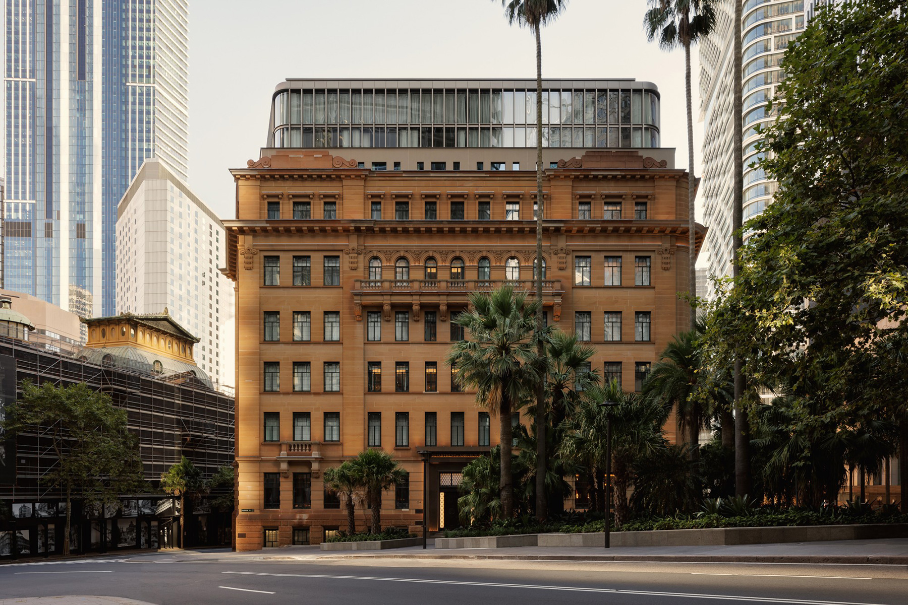 Historic brown brick building with ornate façade and palm trees on the sidewalk, modern glass towers in the background.
