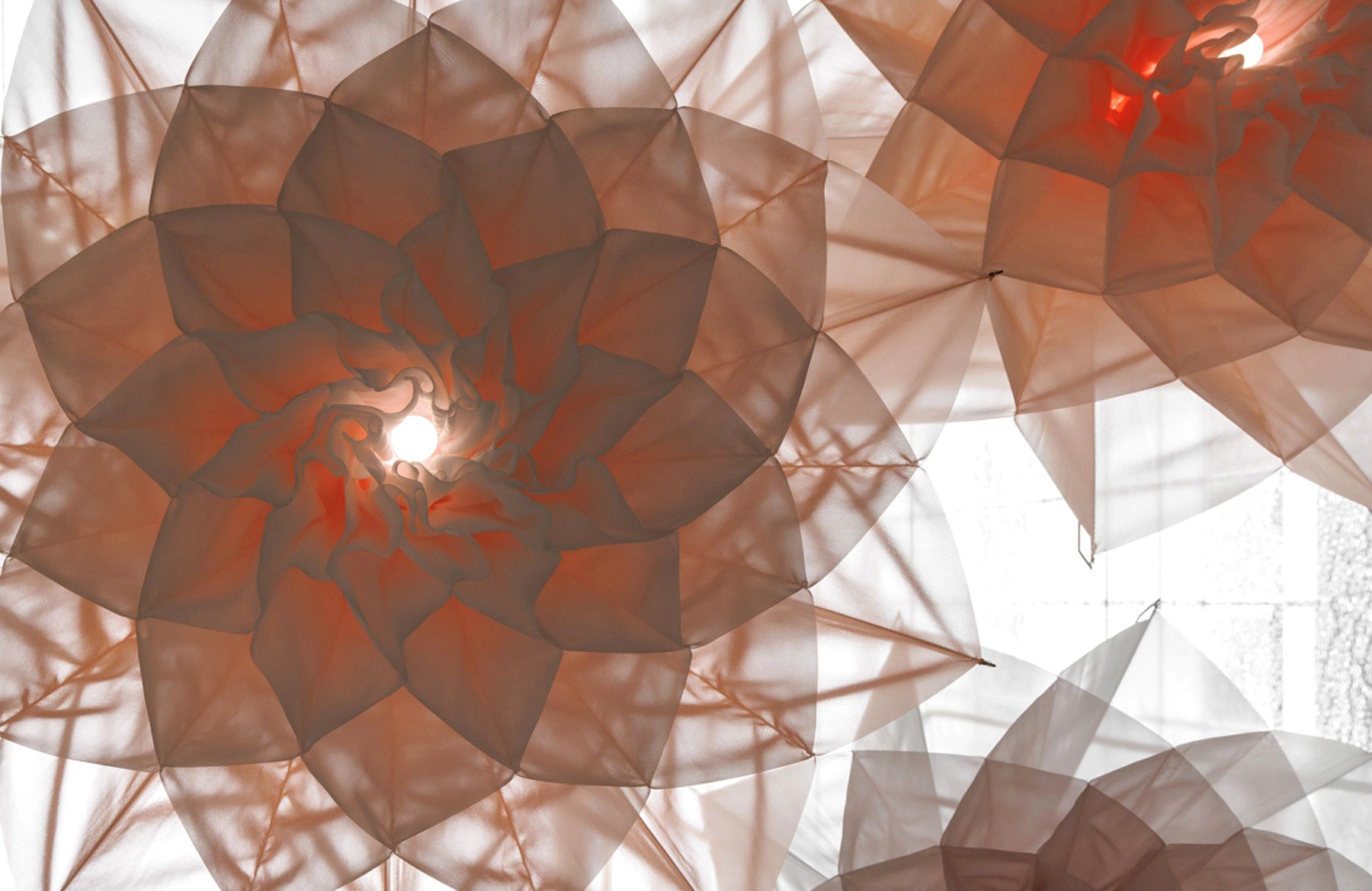 Abstract sculpture of layered translucent orange panels forming a spiraling flower with a backlit center.