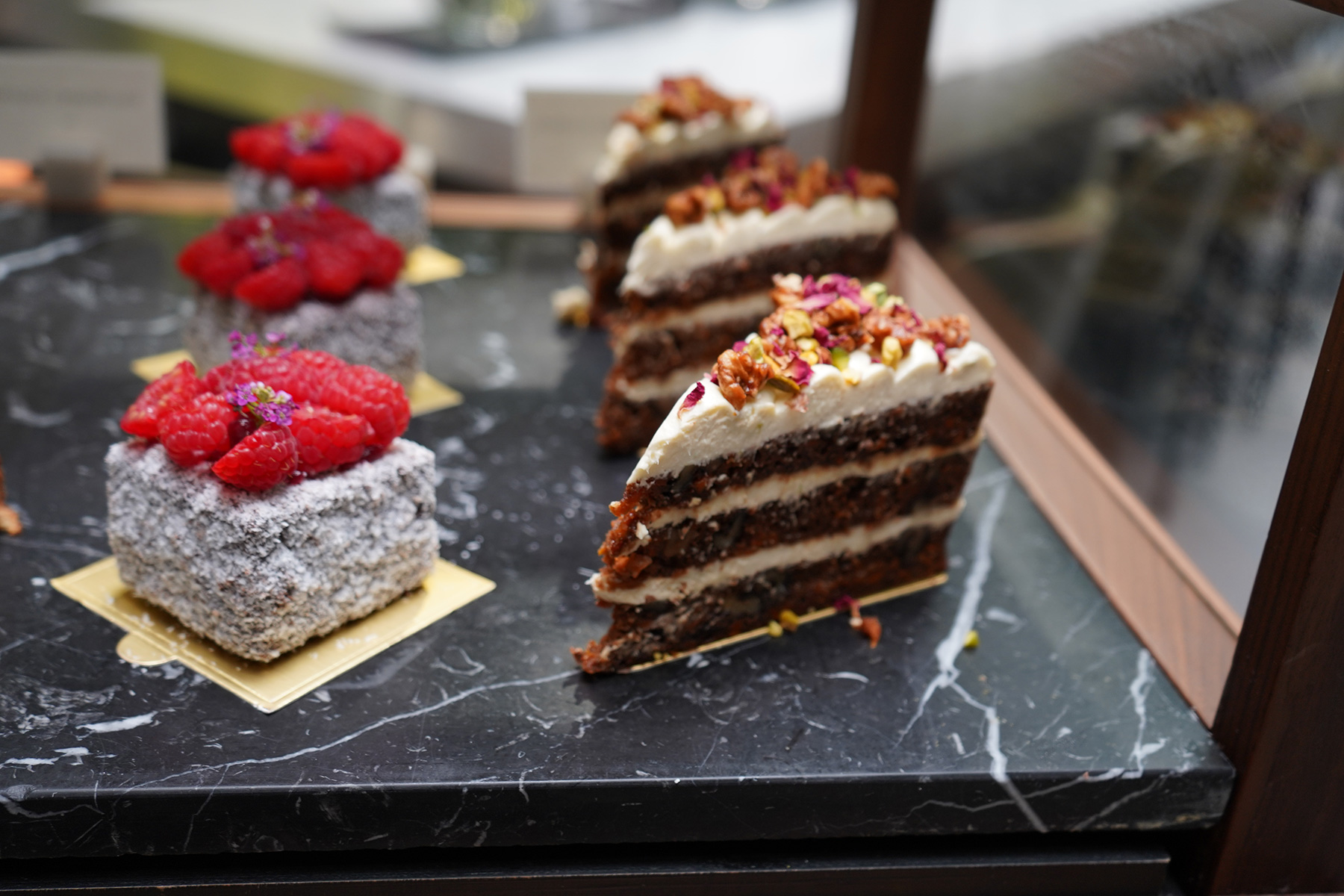 Assorted desserts on a marble counter: raspberry coconut cakes and a multi-layer chocolate cake with cream frosting.