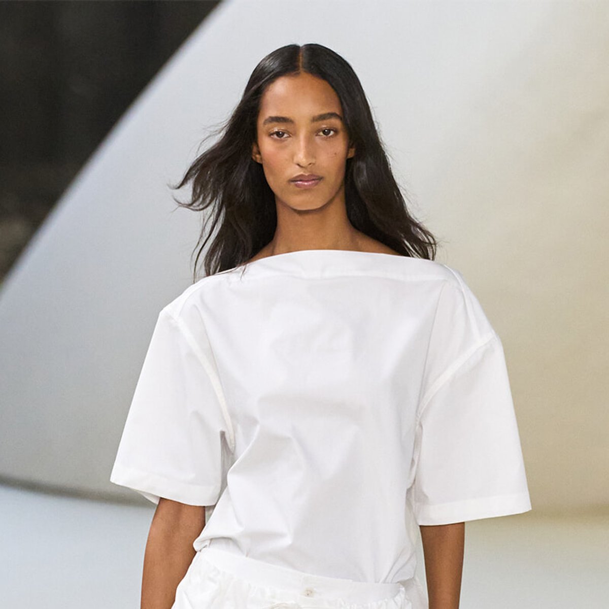 Female runway model wearing an oversized white blouse with wide sleeves against a minimalist background.