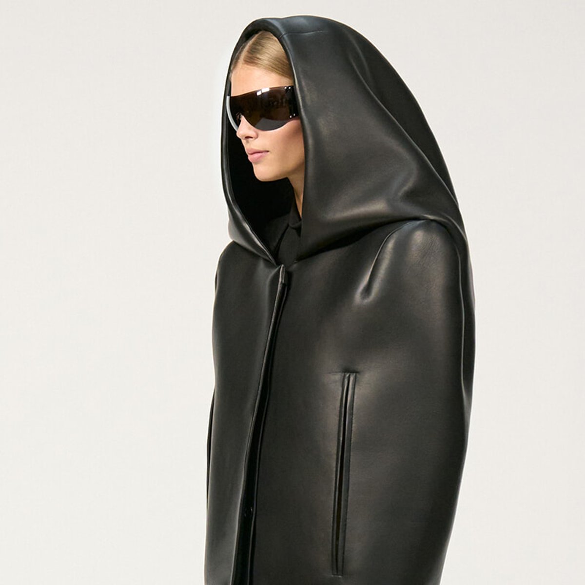 Side view of a person in a black hooded leather coat with oversized sunglasses.
