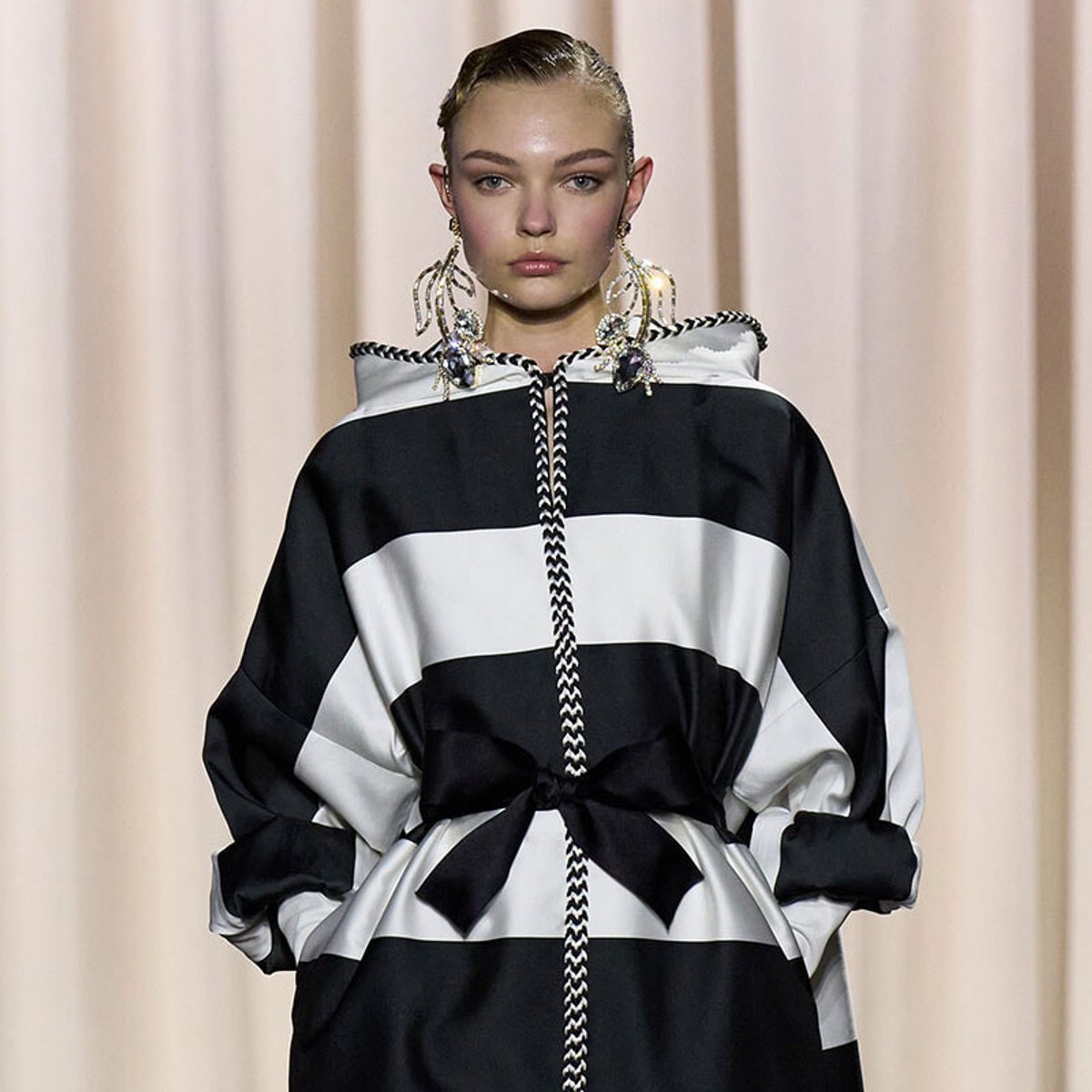 Model on runway wearing a black-and-white striped oversized hoodie dress with a tied waist belt.