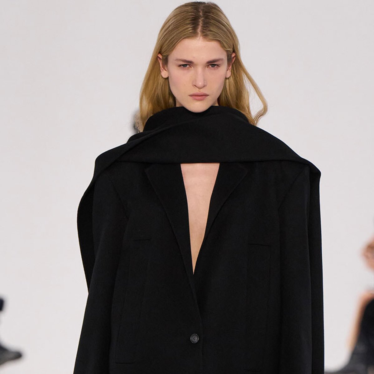 Female model on a runway wearing an oversized black blazer with a deep V back opening and wide lapels.