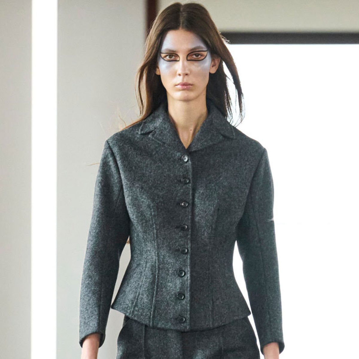 Female model wearing a dark gray, textured blazer with buttons, standing indoors.