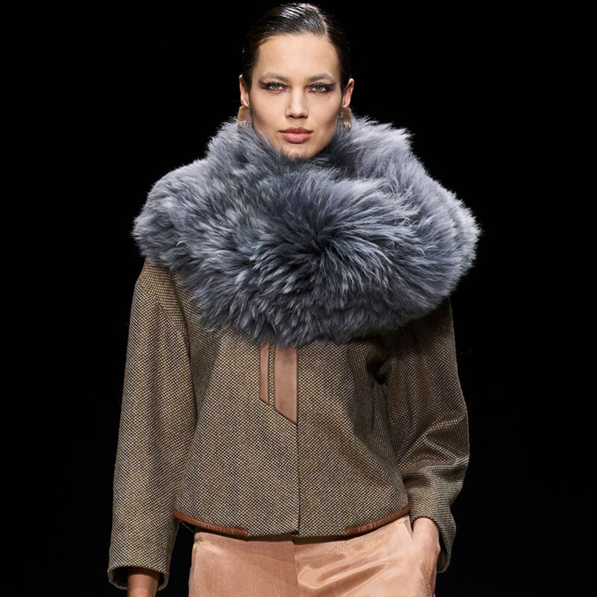 Model on a runway wearing an oversized gray fur collar scarf over a textured brown coat.