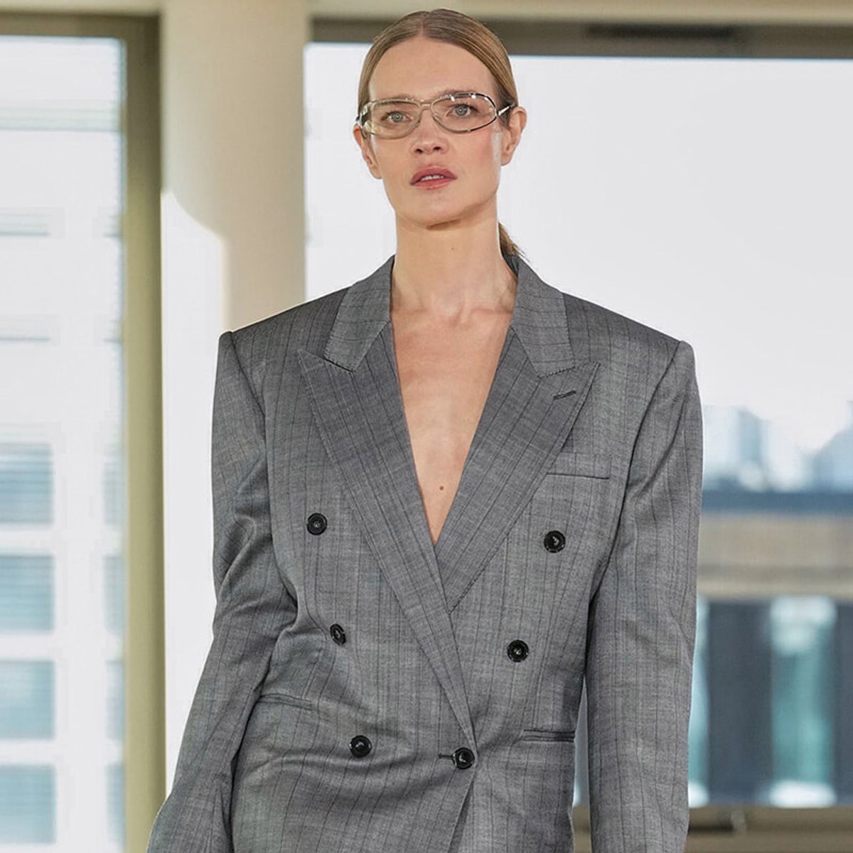 Professionalwoman wearing a gray pinstripe double-breasted blazer and glasses in an office setting.