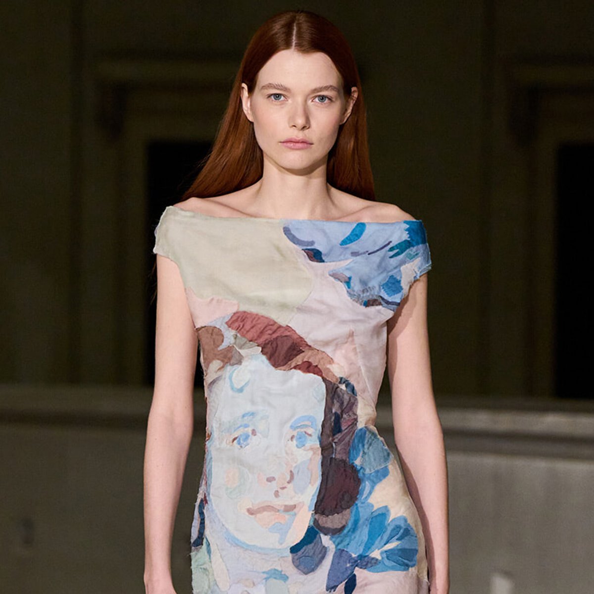 Runway model wearing an off-the-shoulder dress with an abstract blue, beige, and brown painted-print design.