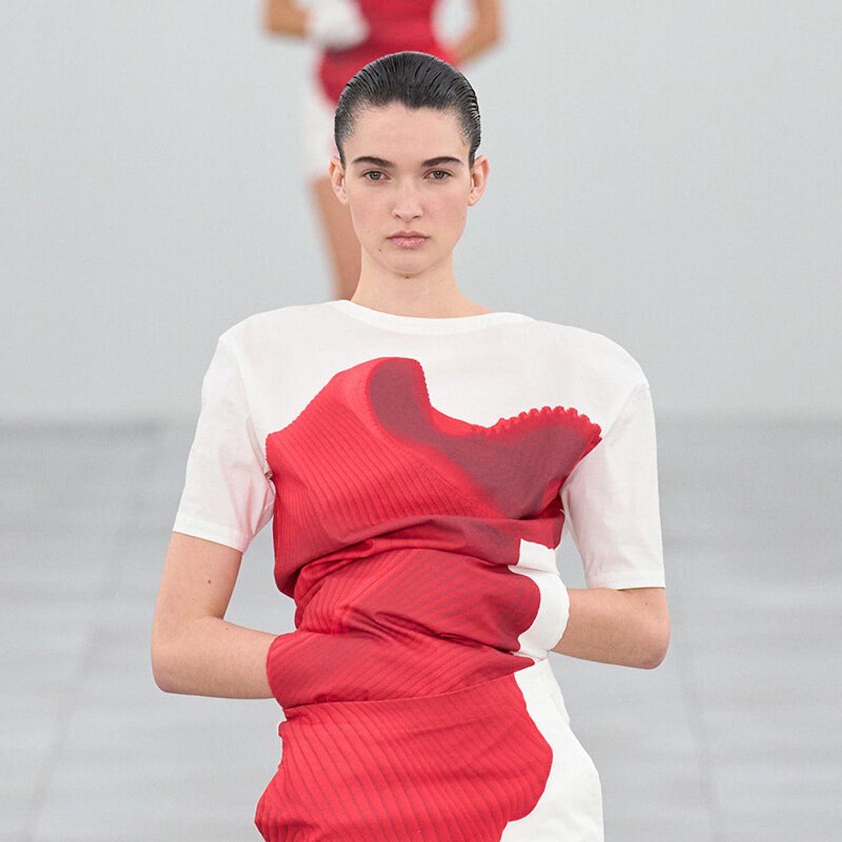 Model walking the runway in a white dress with a bold red abstract pattern across the front.