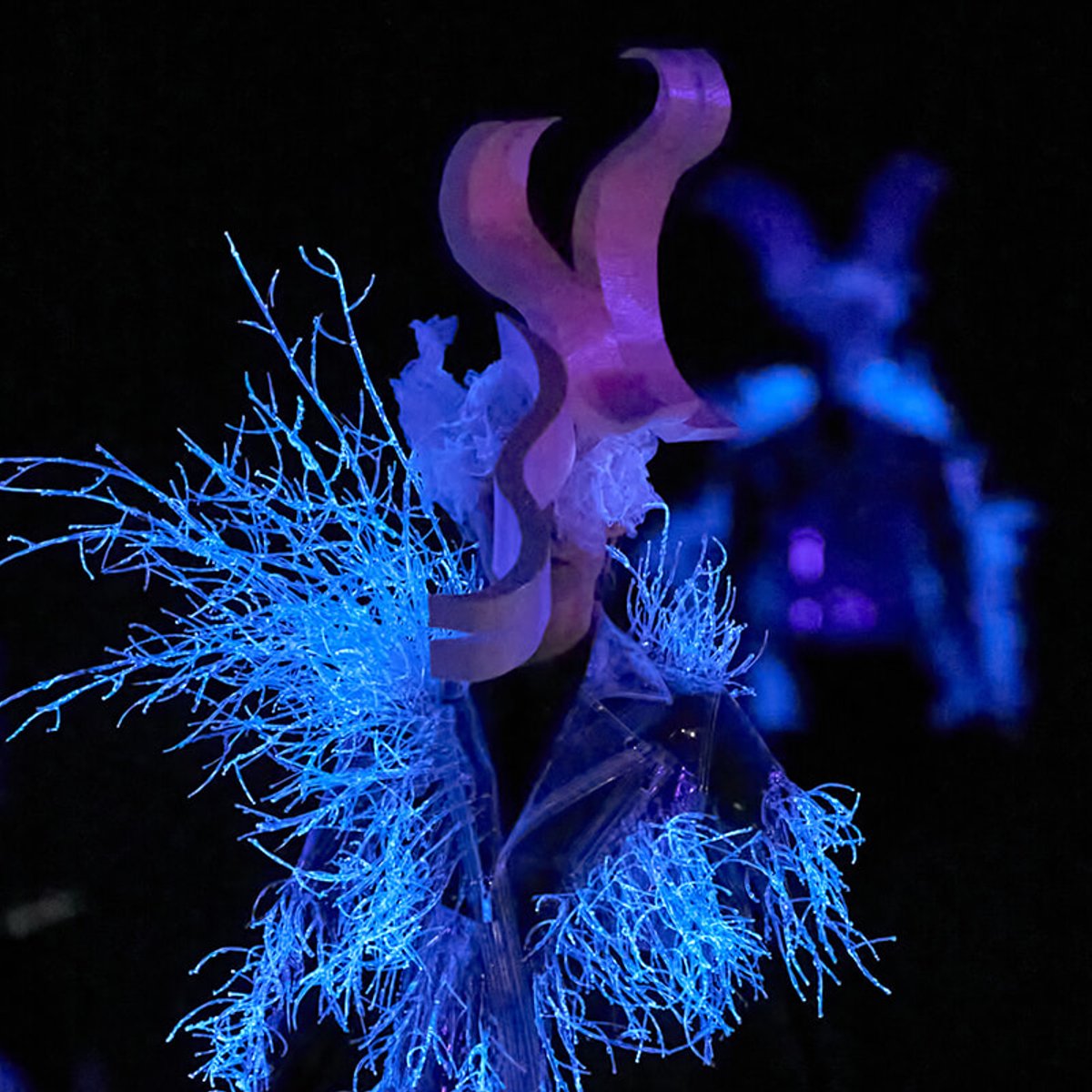 Abstract neon sculpture with blue coral-like branches and purple curled ribbons against a dark background.
