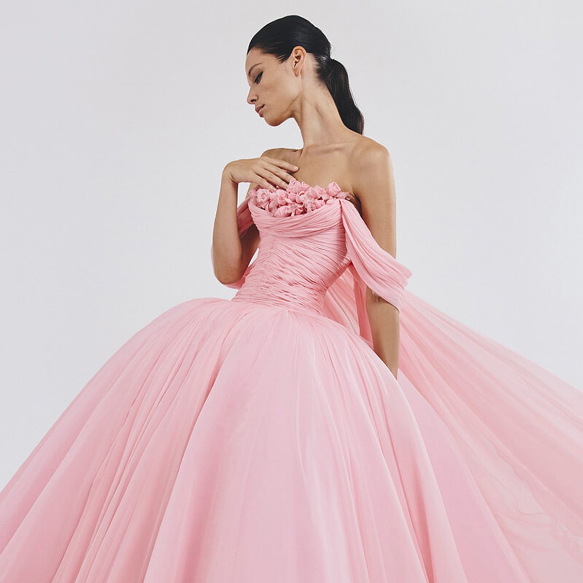 Woman in a pink strapless ball gown with a ruched bodice and flower embellishments, flowing tulle skirt.
