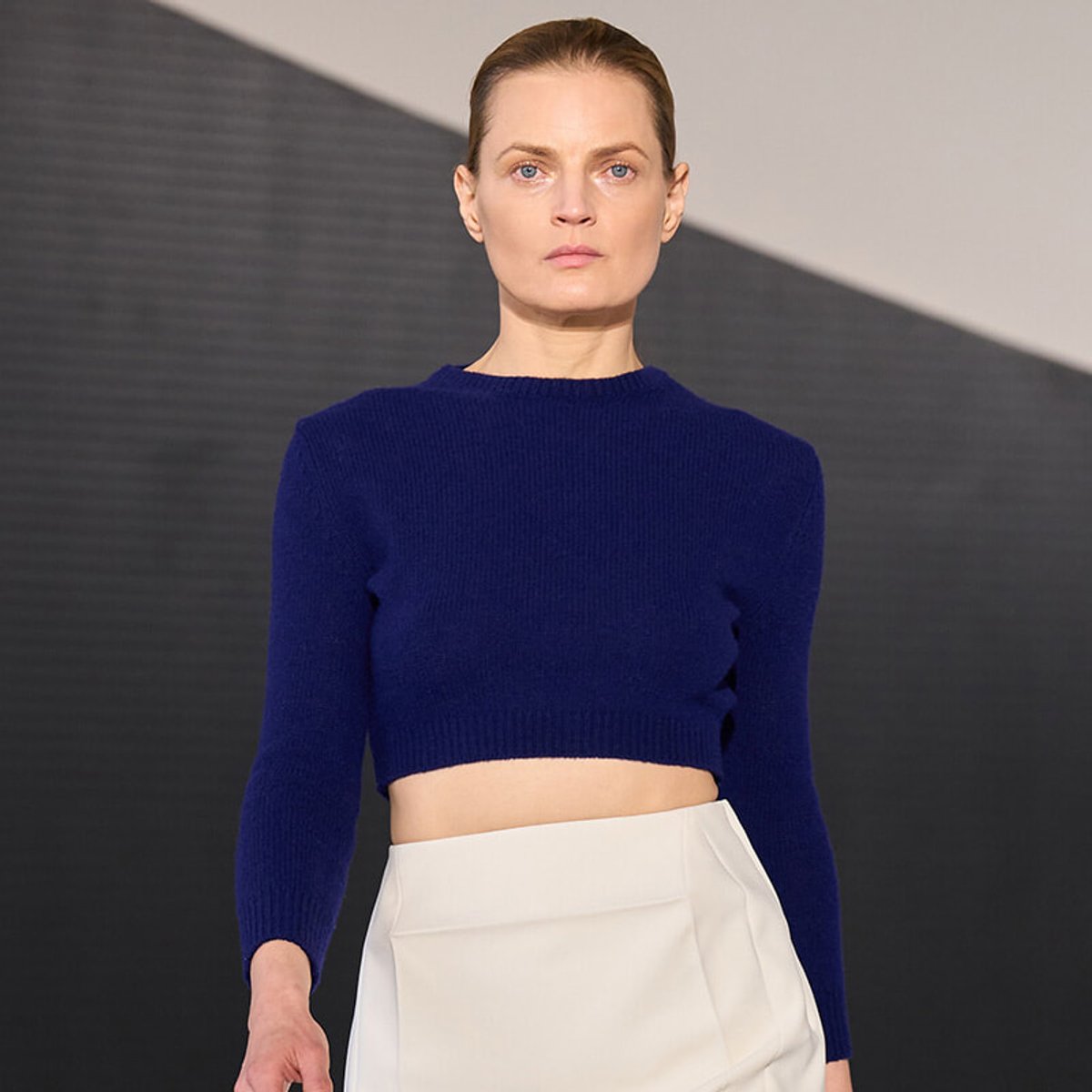 Model walking the runway in a royal blue cropped knit sweater paired with a white high-waisted skirt.