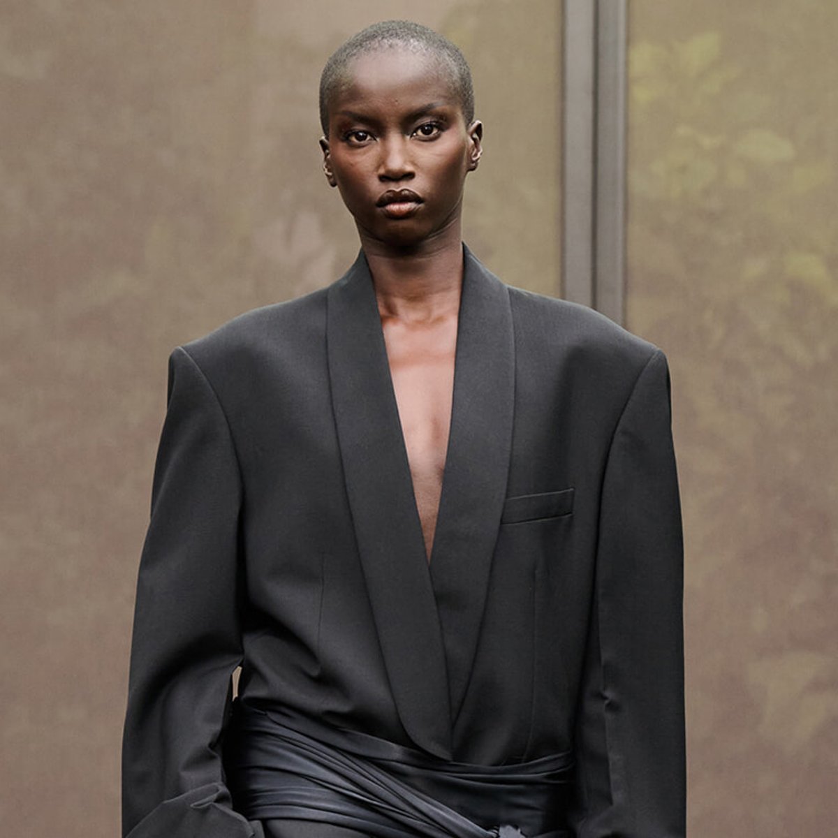 Fashion model wearing a tailored black blazer with a deep plunging neckline and a satin-wrapped waist.