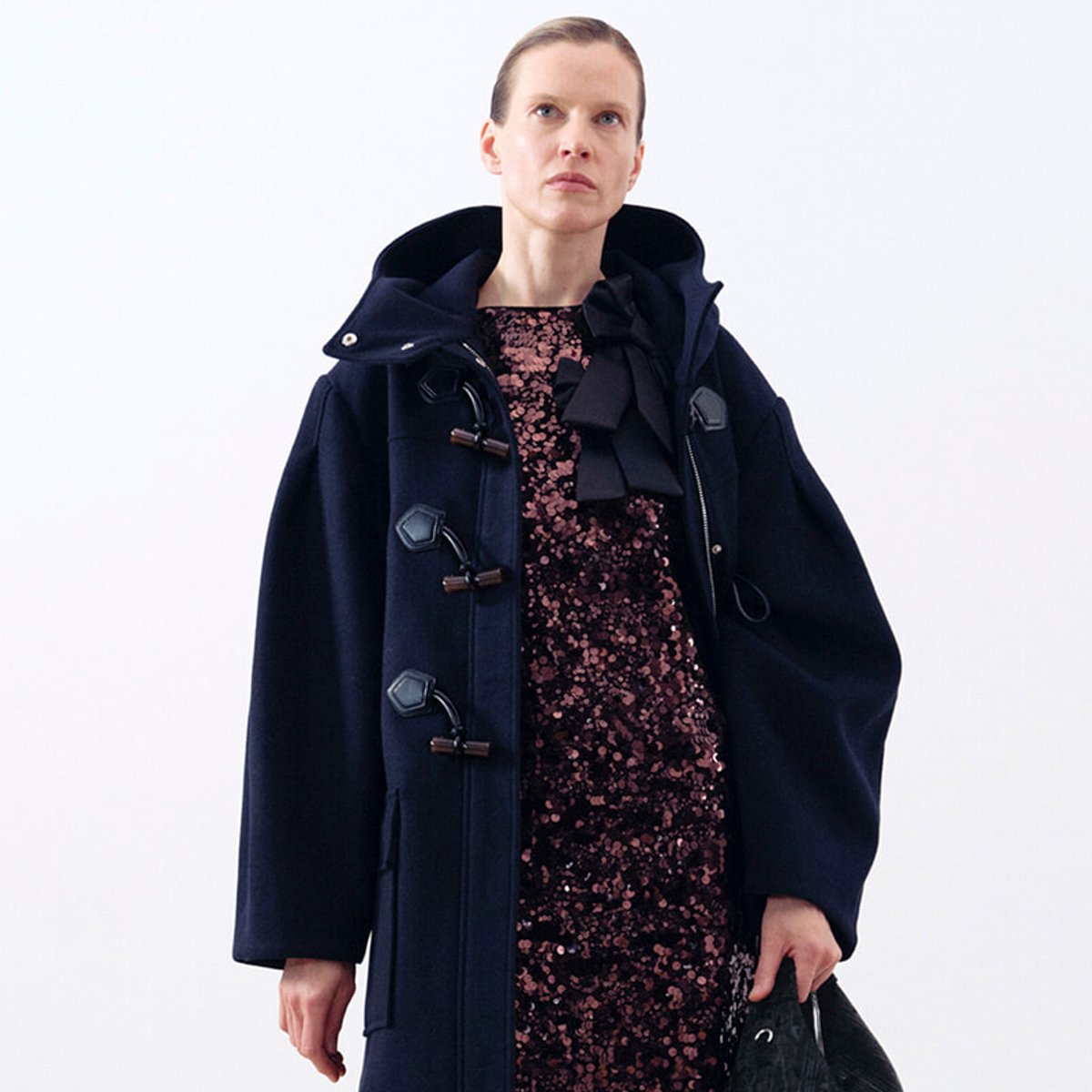 Model wearing a navy duffle coat over a pink sequined dress, facing slightly to the left.