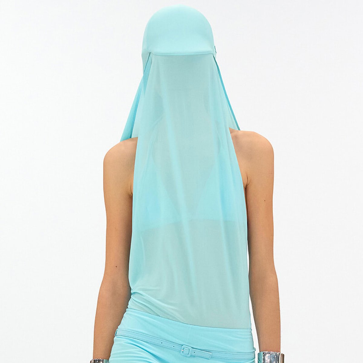 Back view of a person wearing a light blue headscarf draped over the head and shoulders with a matching sleeveless top against a white background.