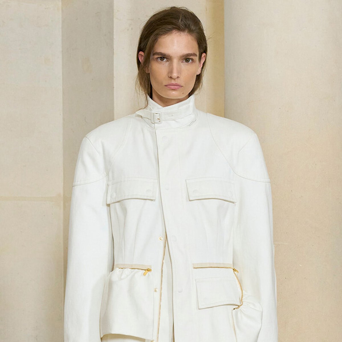 Model wearing an oversized white utility jacket with a high collar and large front pockets against a neutral backdrop.