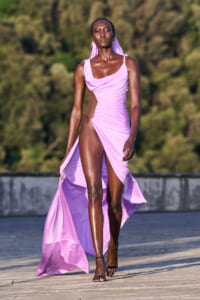 Model walking on a runway in a flowing lavender dress with a high slit, outdoors.