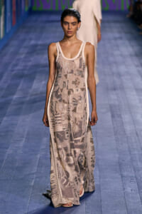 Model walks the runway in a sleeveless, beige sequin maxi dress with abstract metallic patterns on a blue catwalk surface.
