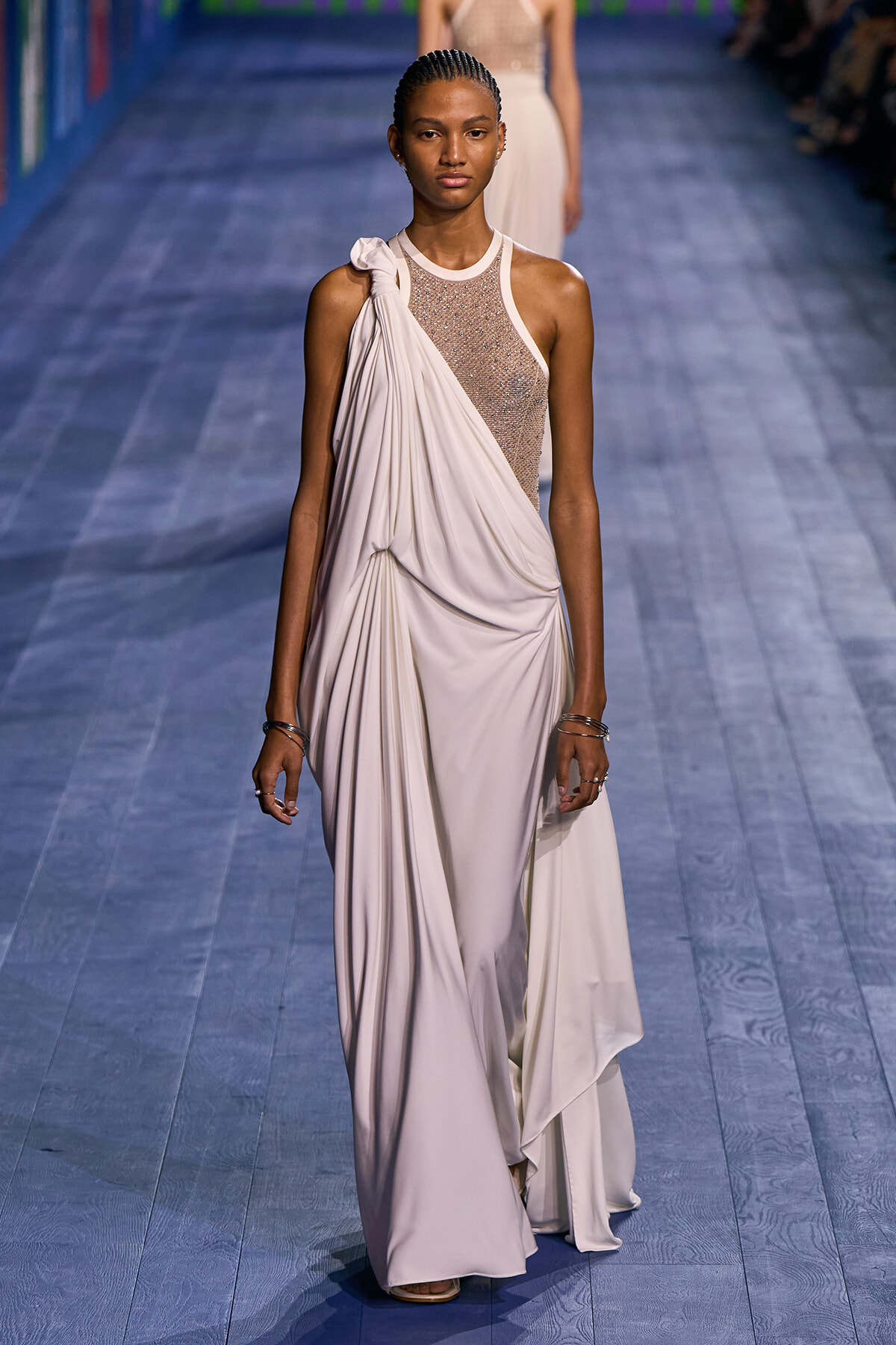 Model walks the runway in a cream draped gown with a beaded mesh bodice and one-shoulder detail.