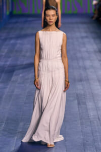 Model walking the blue runway in a pale pink sleeveless pleated floor-length gown.