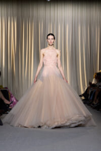 Model on runway wearing a strapless blush pink tulle ballgown with a floral bodice.