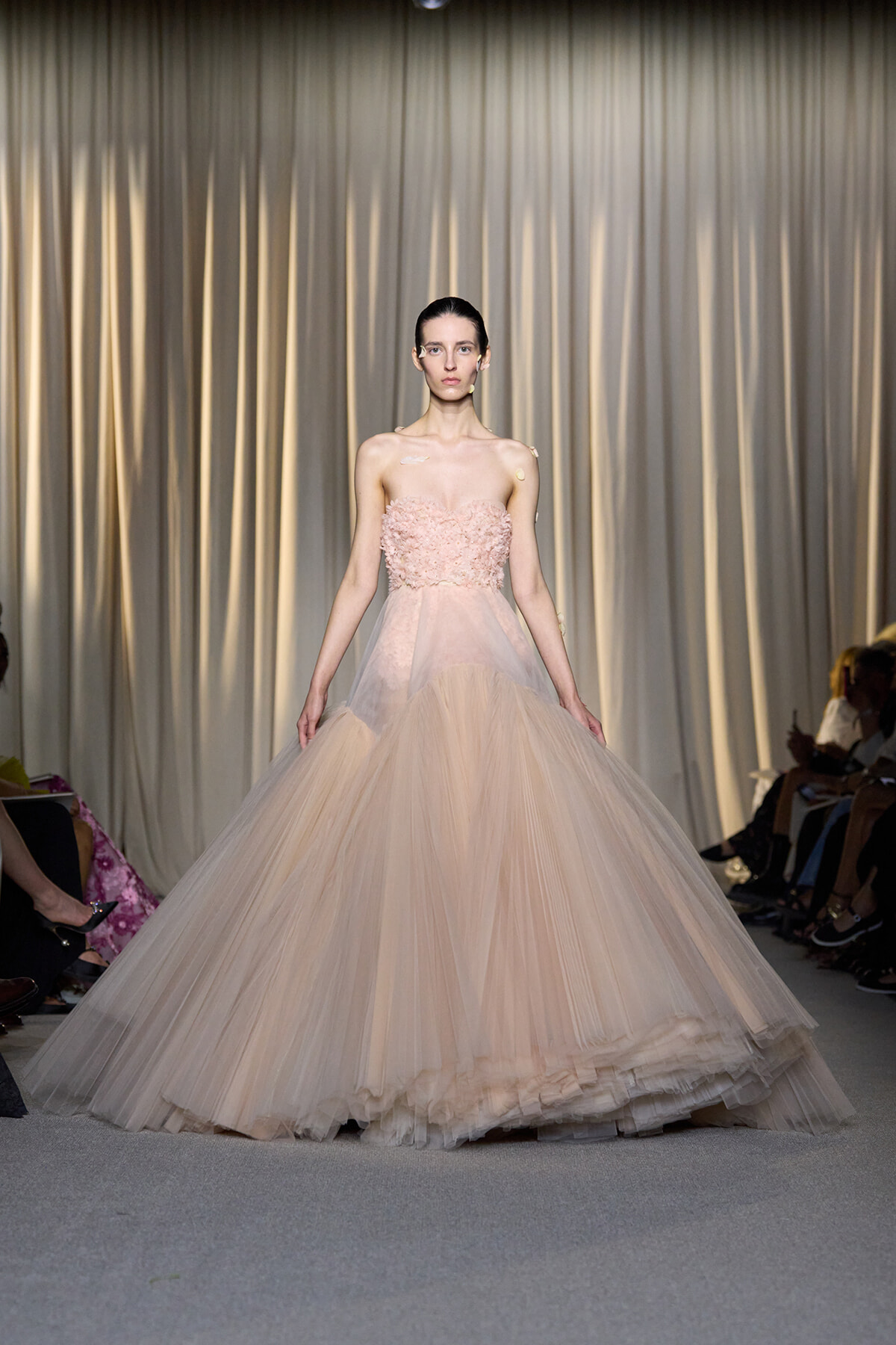 Model on runway wearing a strapless blush pink tulle ballgown with a floral bodice.