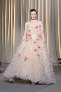 Fashion model on a runway wearing a voluminous pale pink floral gown with pink rose appliqués and a strapless bodice.