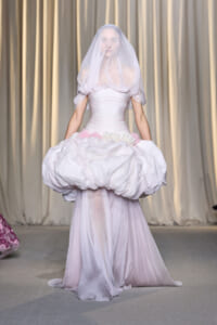 Model walks the runway in a pale pink wedding gown with a voluminous bubble skirt and translucent veil.