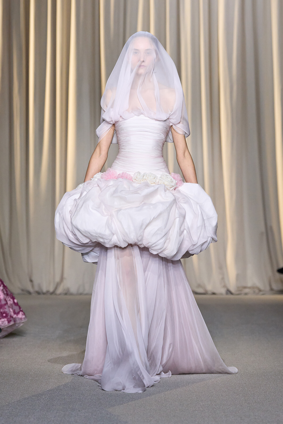 Model walks the runway in a pale pink wedding gown with a voluminous bubble skirt and translucent veil.