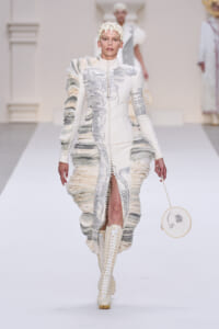Runway look: an all-white sculptural coat with silver paneling, heavy textured ruffles, and cream lace-up boots.