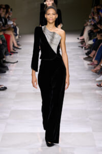 Model walks the runway in a black velvet one-shoulder gown with a silver beaded, draped bodice.