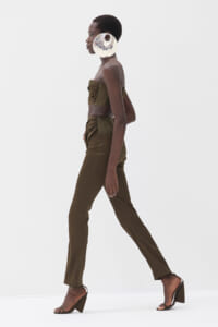 Profile view of a model walking in an olive-green strapless top and matching high-waisted pants, with a large circular metallic earring.
