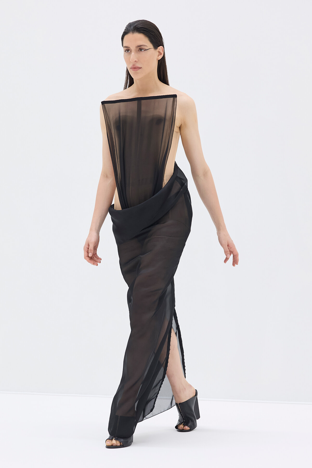 Model wearing a black sheer evening gown with a draped overlay, one-shoulder neckline, and a side slit.