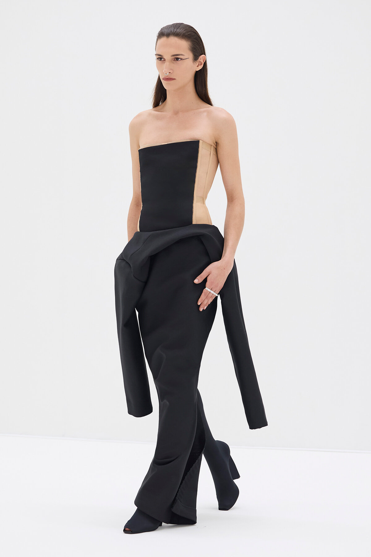Model wearing a strapless color-block bodice (black front with beige sides) paired with avant-garde black draped pants in a studio setting.