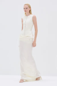 Model wearing a sleeveless ivory textured bodice and flowing cream satin skirt in a white studio setting.