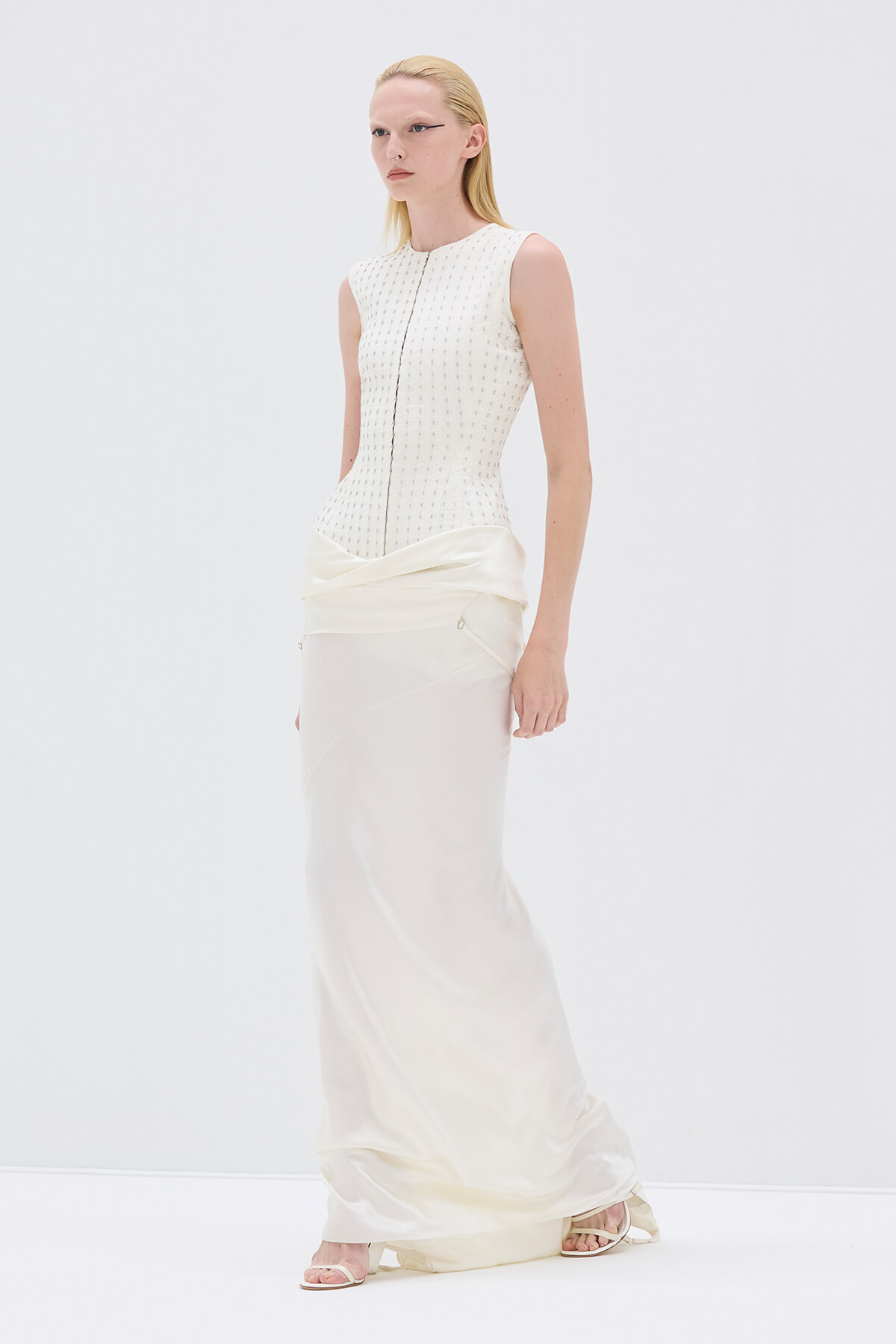 Model wearing a sleeveless ivory textured bodice and flowing cream satin skirt in a white studio setting.