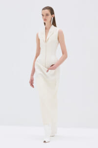 Ivory sleeveless dress with a plunging lapel collar, front zipper, and side pockets, paired with white knee-high heeled boots in a studio setting