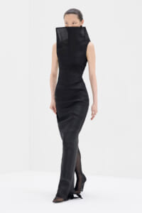 Full-length black sleeveless gown with a tall sculptural collar covering the lower face, worn by a model in a white studio.