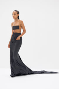 Model wearing a black strapless top and a floor-length satin gown with a long train against a white studio background.