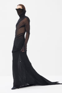 Model in a sheer black mesh top and long black gown with a sweeping train, posing against a white studio background.
