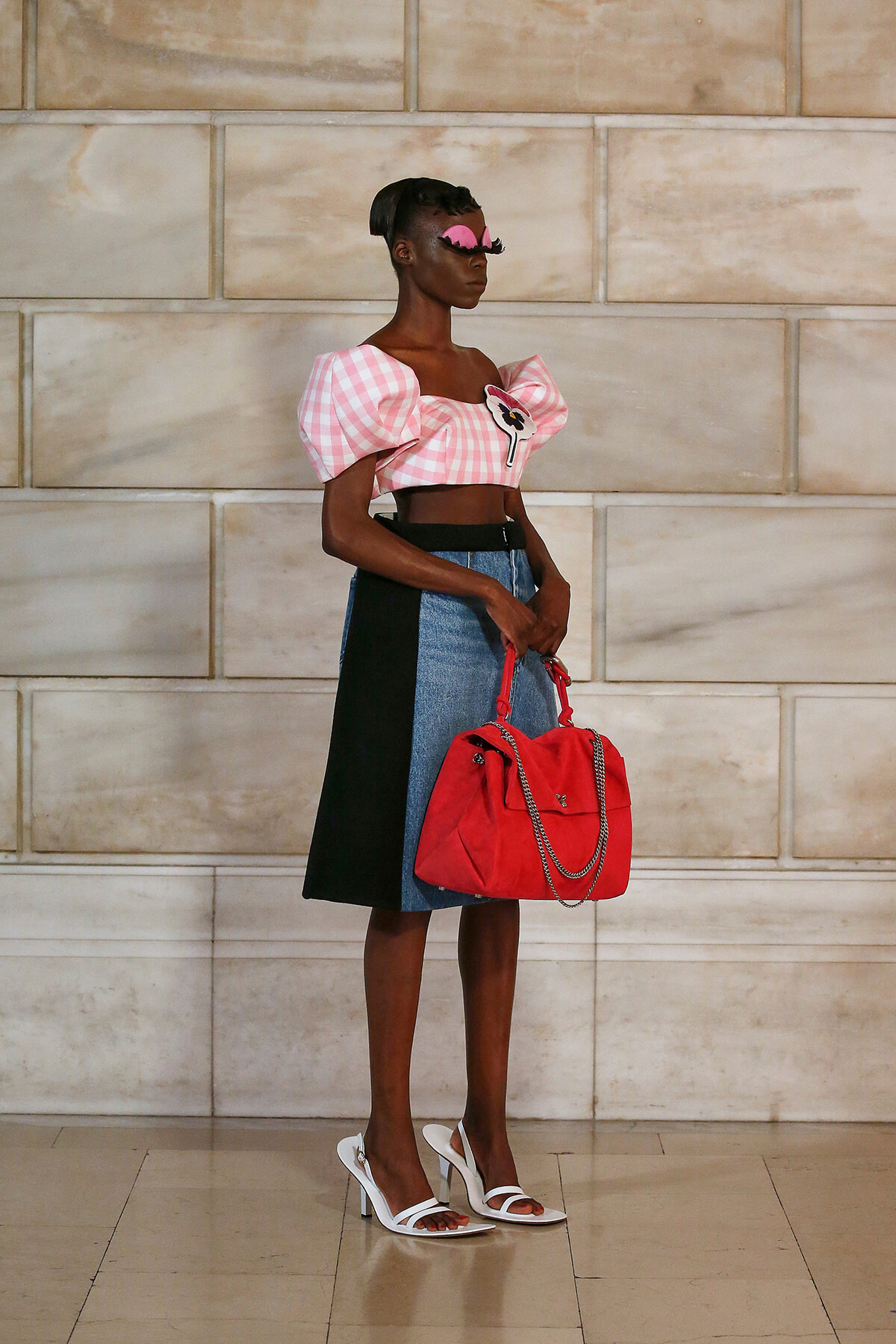 Model in a pink gingham puff-sleeve crop top, color-block denim skirt, white heeled sandals, pink mask, and a red handbag with a chain strap.