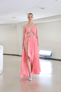 Female model in a pink strapless dress with cutouts and a high slit, standing in a bright studio.