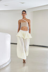 Model walking a runway in a beige bandeau top and flowing white layered trousers in a minimalist setting.
