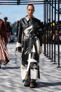 Model walks the runway in a long black-and-white abstract-print coat tied at the waist.