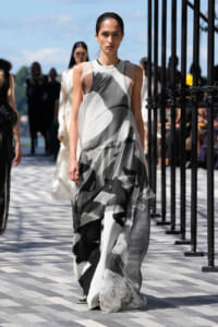 Model walks the runway in a sleeveless, floor-length dress with an abstract black-and-gray brushstroke pattern outdoors.
