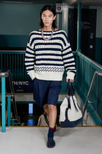 Model walking down stairs in a navy and white striped knit sweater, navy shorts, and blue tote bag.
