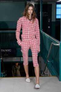 Model walking the runway in a pink plaid matching shirt and knee-length shorts, white woven slip-ons.